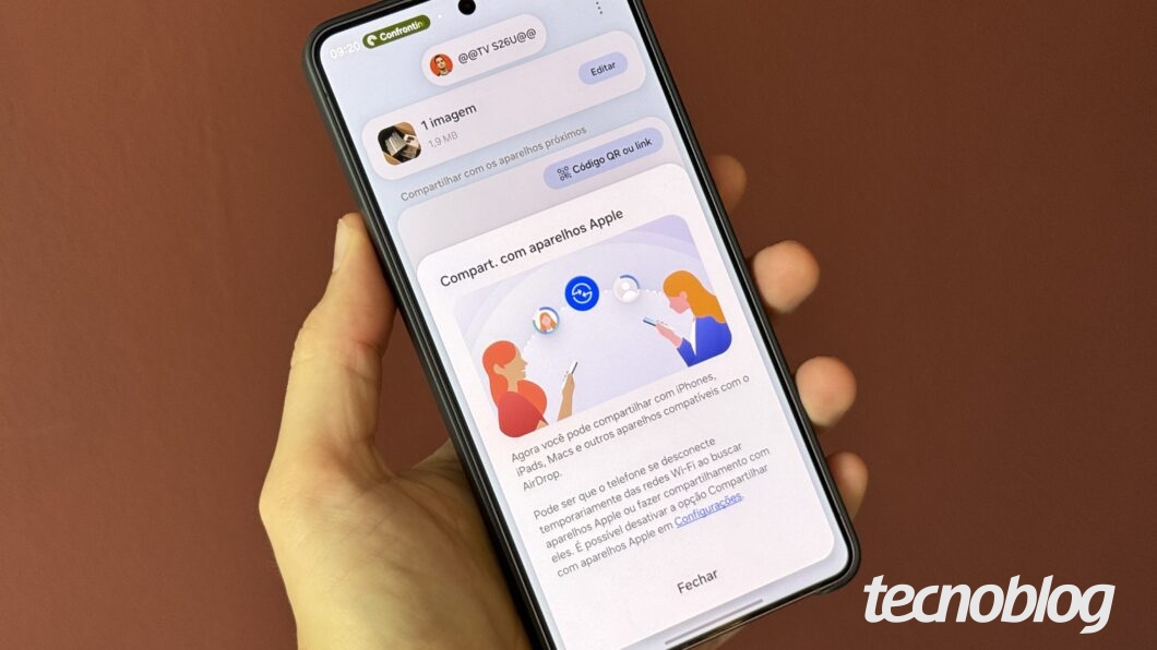 Mão segurando celular, com aviso de compartilhamento na tela