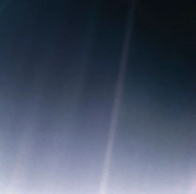 Earth appears as a tiny bright dot inside a faint vertical beam of scattered sunlight against the dark blue-black background of space.