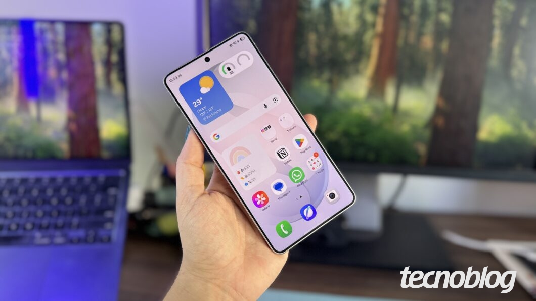 Mão segurando Galaxy S26 Ultra; celular está com a tela ligada e exibe ícones de apps na interface One UI 8.5