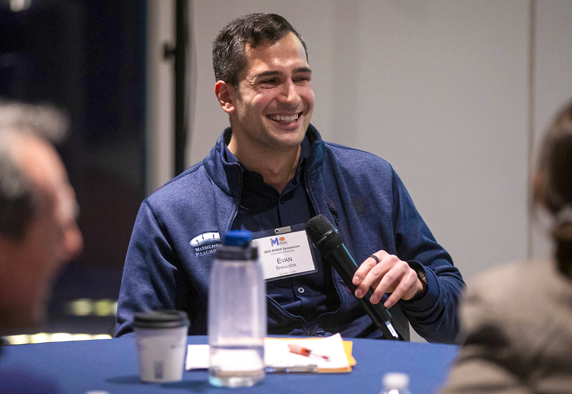 Evan Shaulson smiles while holding a microphone.