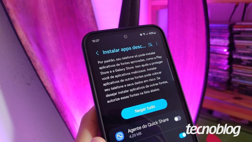 Uma mão segura um celular Samsung na tela "Instalar apps desconhecidos"