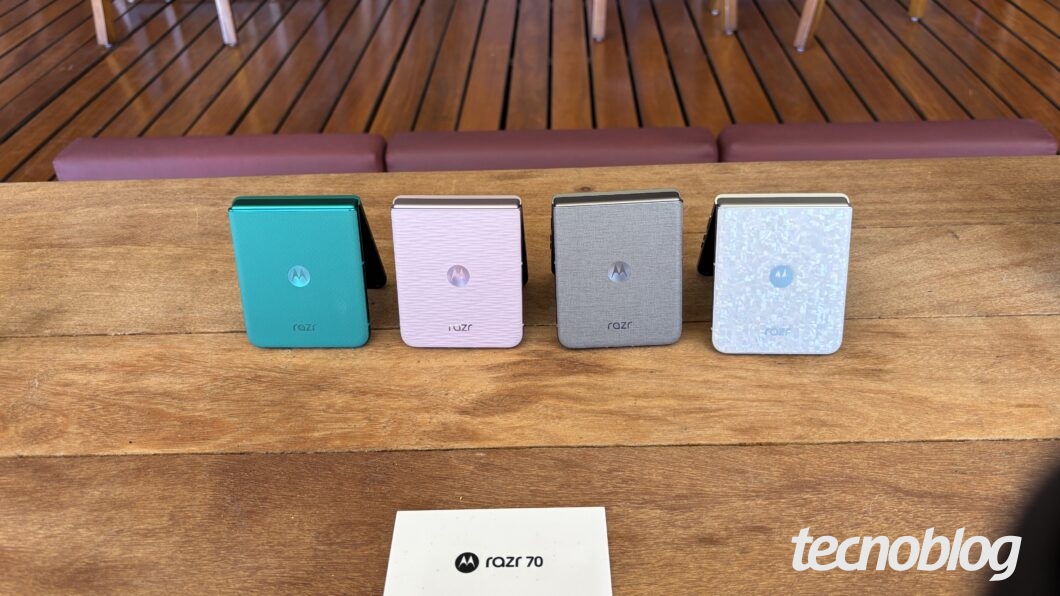 Quatro celulares Motorola razr 70 em cores azul, rosa, cinza e translúcida sobre uma mesa de madeira