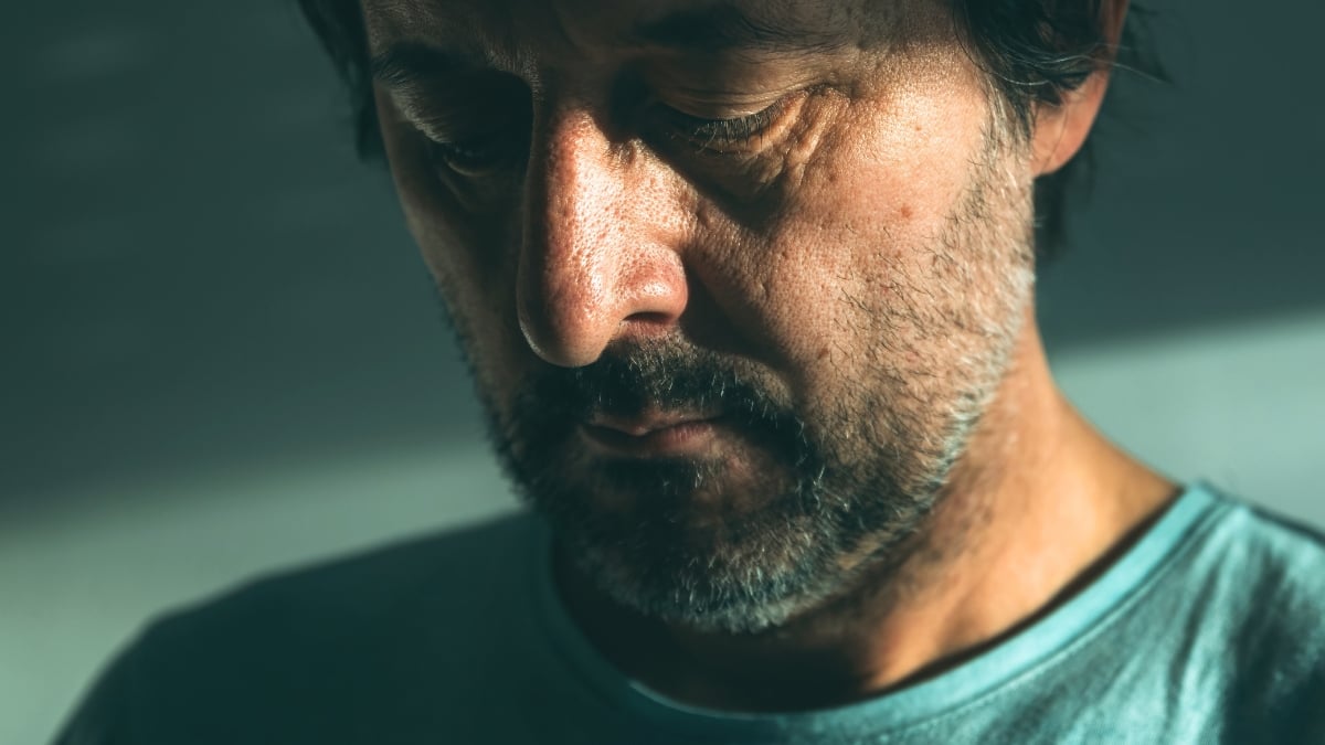 Depressed looking man in his 40s with brown hair gazing downward