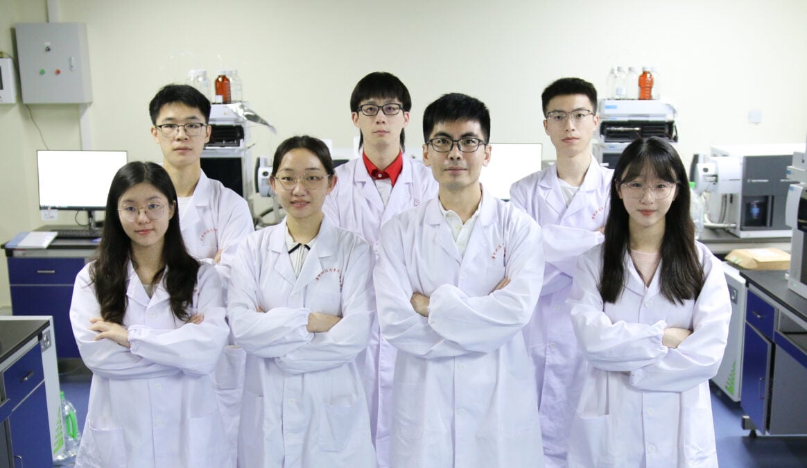 Seven members of Dr. Shan's research group wearing white lab coats in a laboratory.