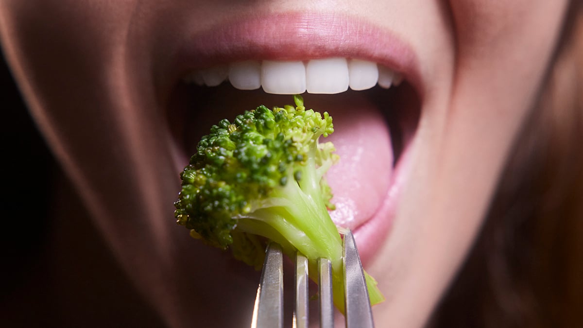 Young woman mouth eating broccoli