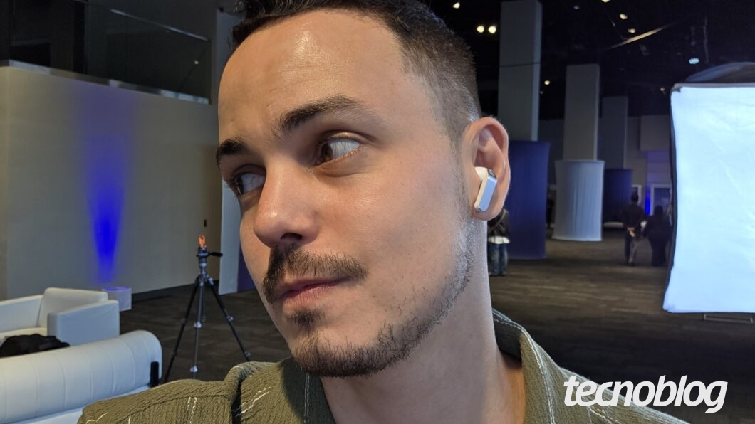 Close de um homem usando um dispositivo auditivo sem fio, em estúdio com luzes e equipamentos ao fundo