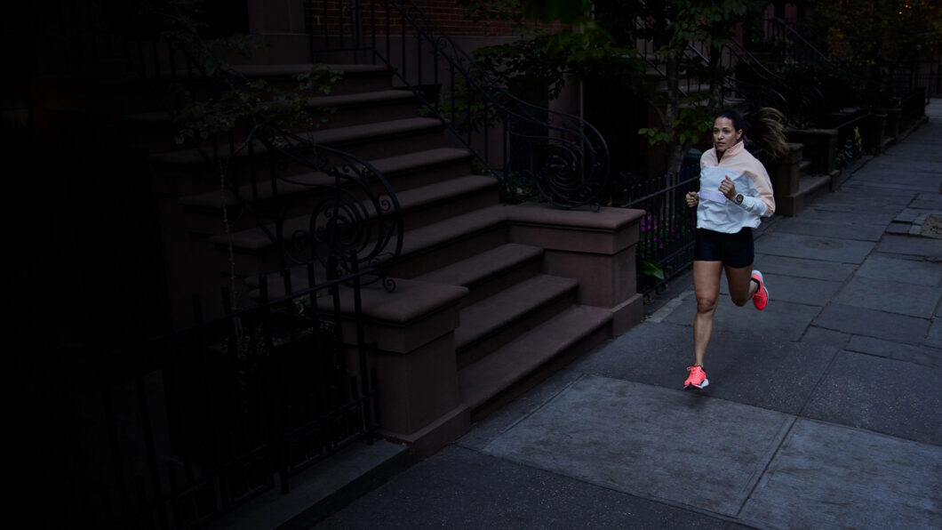 Corredora usando o smartwatch Garmin Forerunner 965 durante treino em uma rua urbana