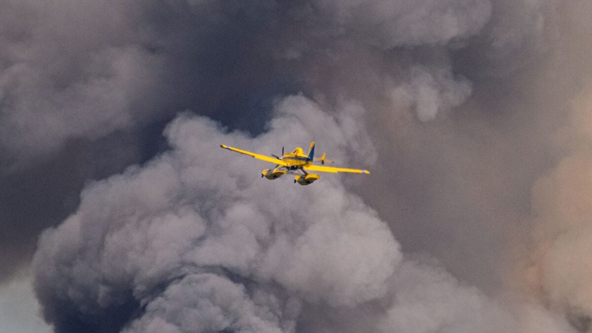 Dramatic scene of a yellow airplane flying through dense smoke, possibly from a wildfire