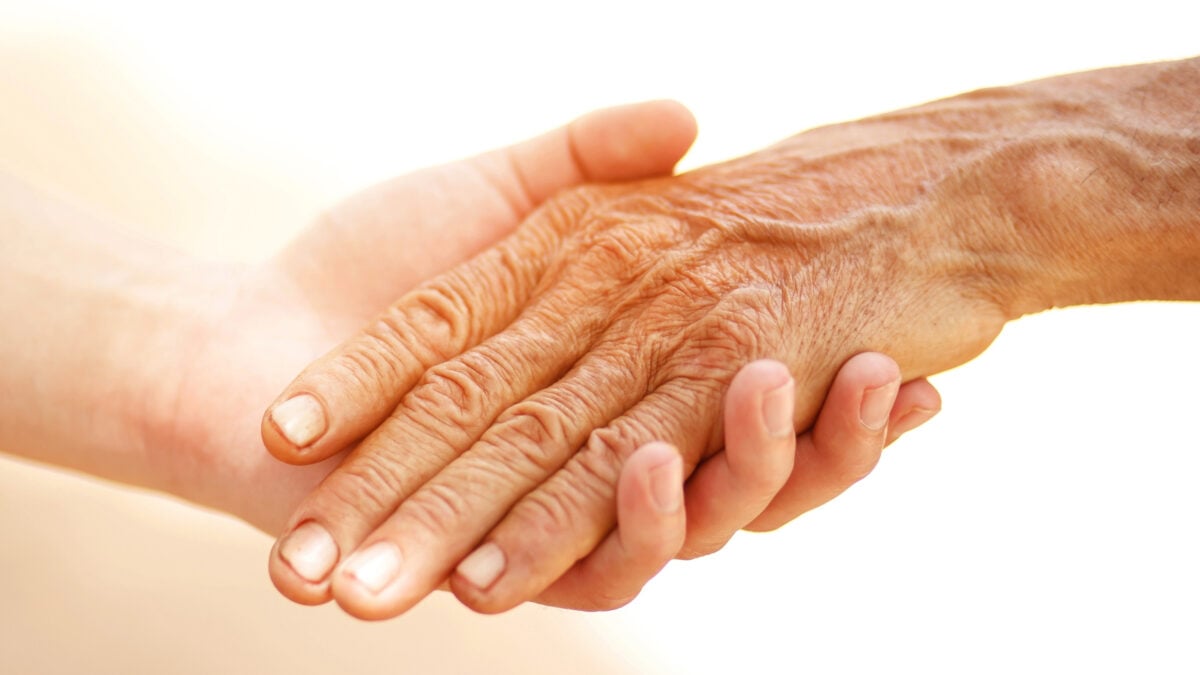 young person's hand holding the hand of an elderly person